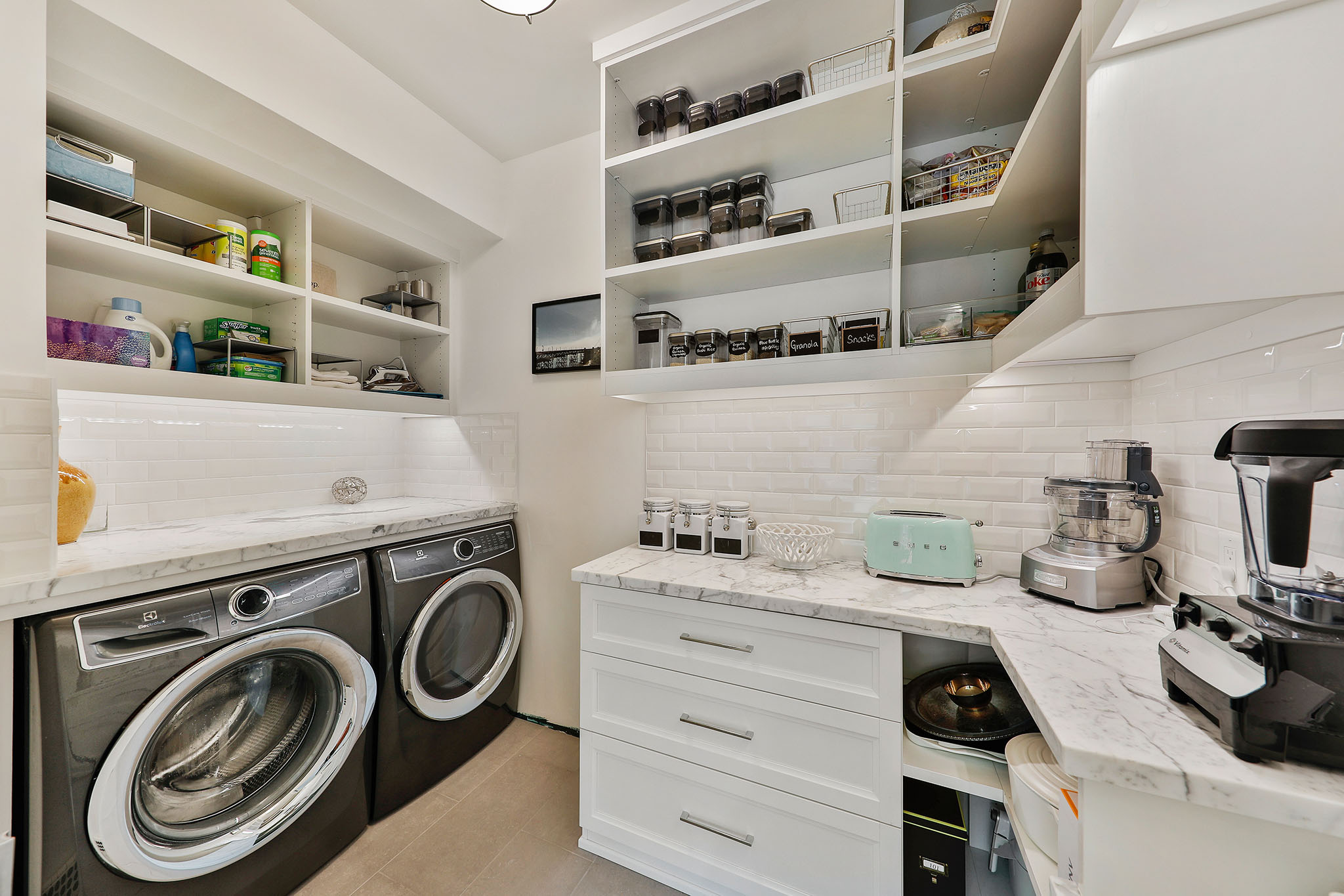 Full sized washer and dryer housed in the walk-in pantry, outfitted with marble counters